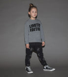 A child standing against a gray background, wearing black baggy pants with a star pattern and a gray long-sleeve top with the text 'LIMITED EDITION' printed on the front.