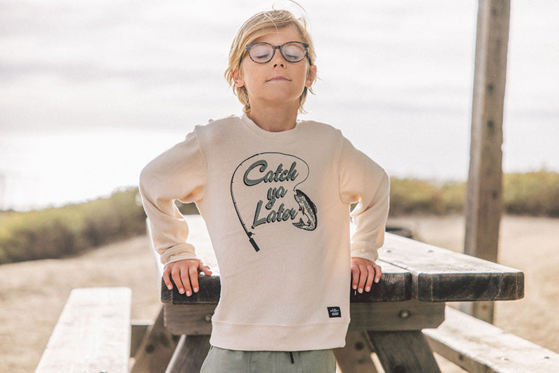 Person wearing a beige sweatshirt with text and graphics, standing outdoors near a picnic table.