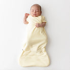 Newborn baby wrapped in a yellow sleep sack on a white background