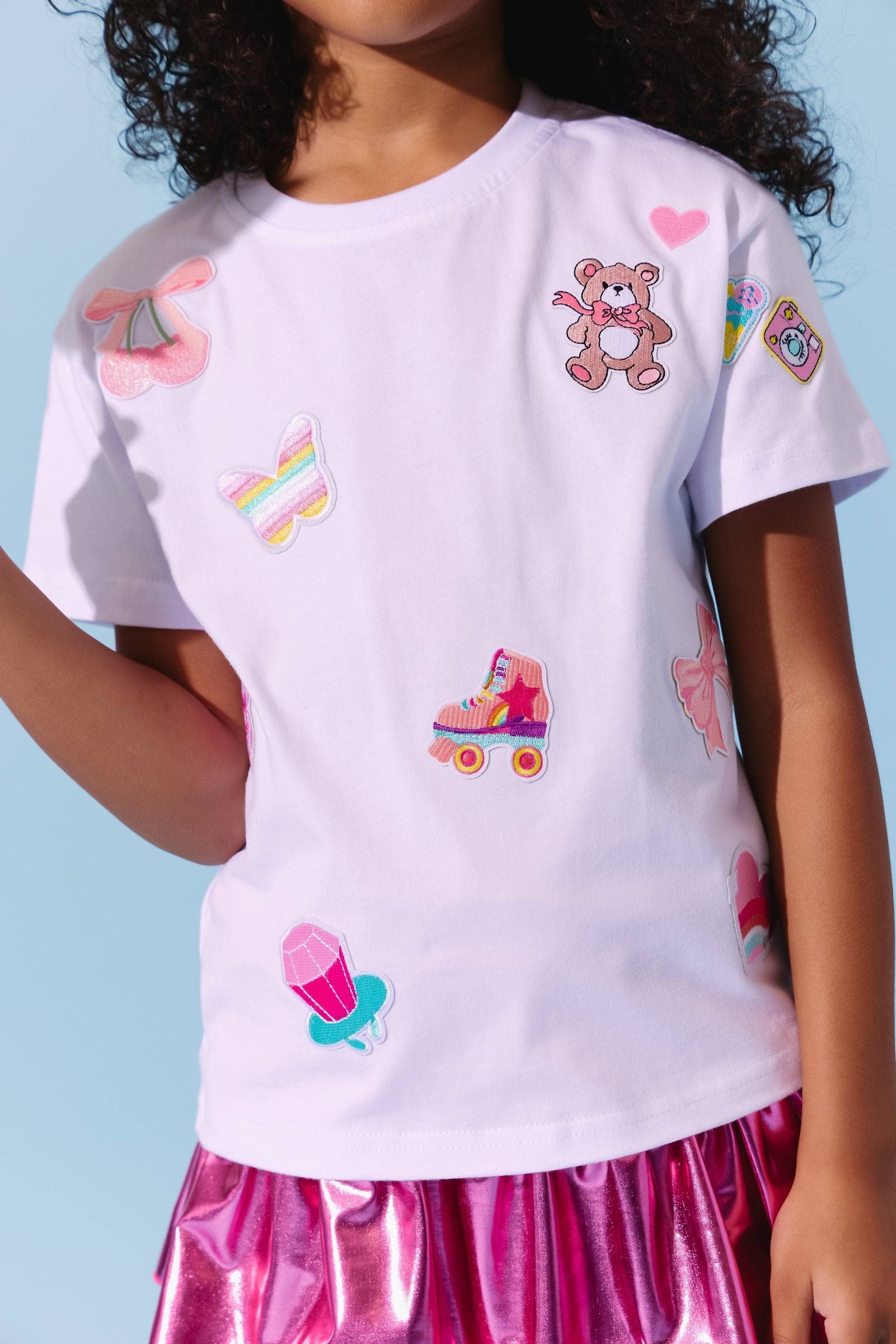 Child wearing a white t-shirt with colorful embroidered designs on a blue background