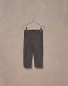 A pair of dark grey, textured cotton baby pants hanging on a hanger against a plain background.