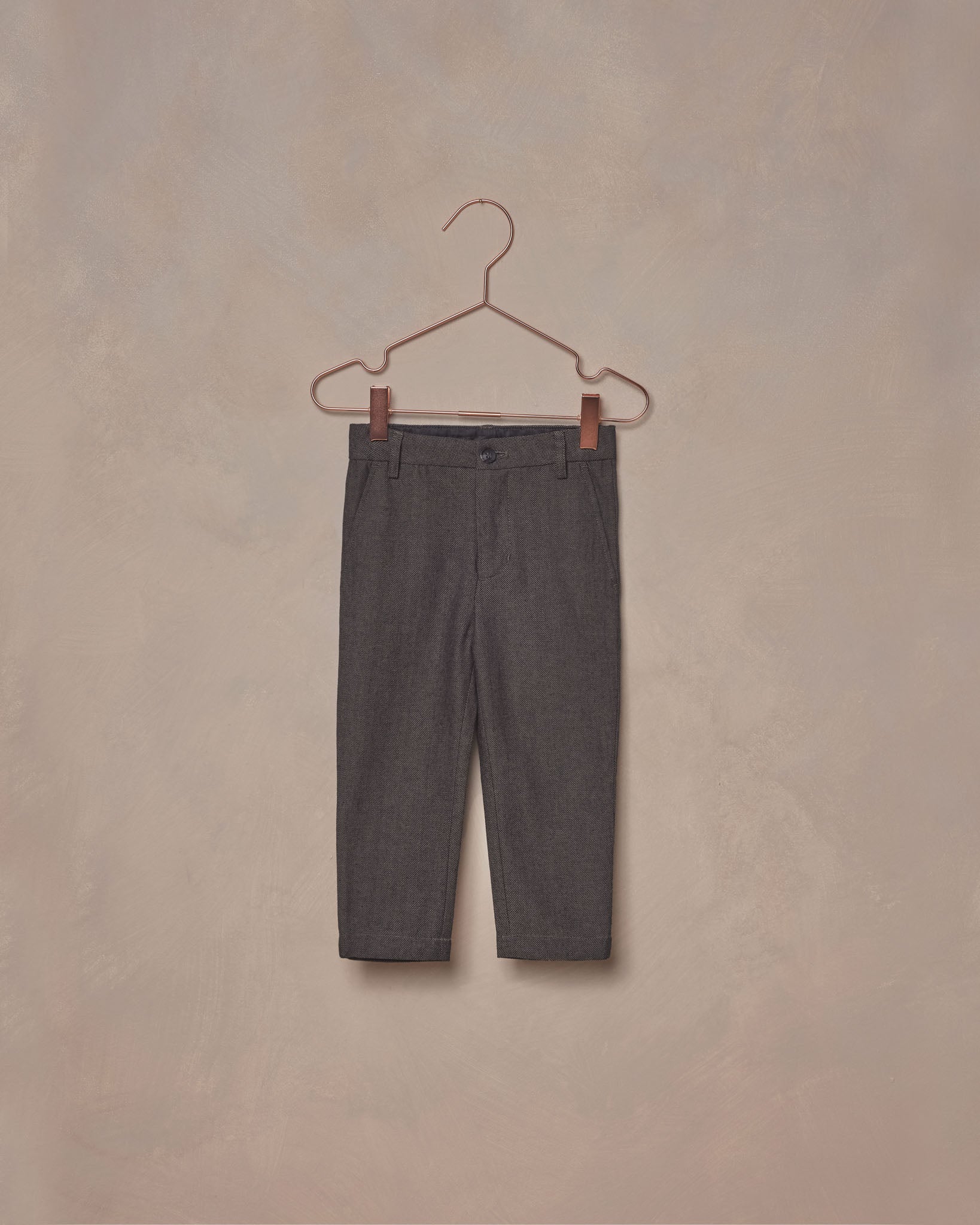 A pair of dark grey, textured cotton baby pants hanging on a hanger against a plain background.