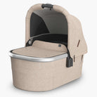 A beige UPPABABY Bassinet V3 with a sunshade, mesh panels, and a carry handle.