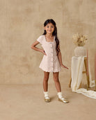 Young girl in a light dress standing against a beige background