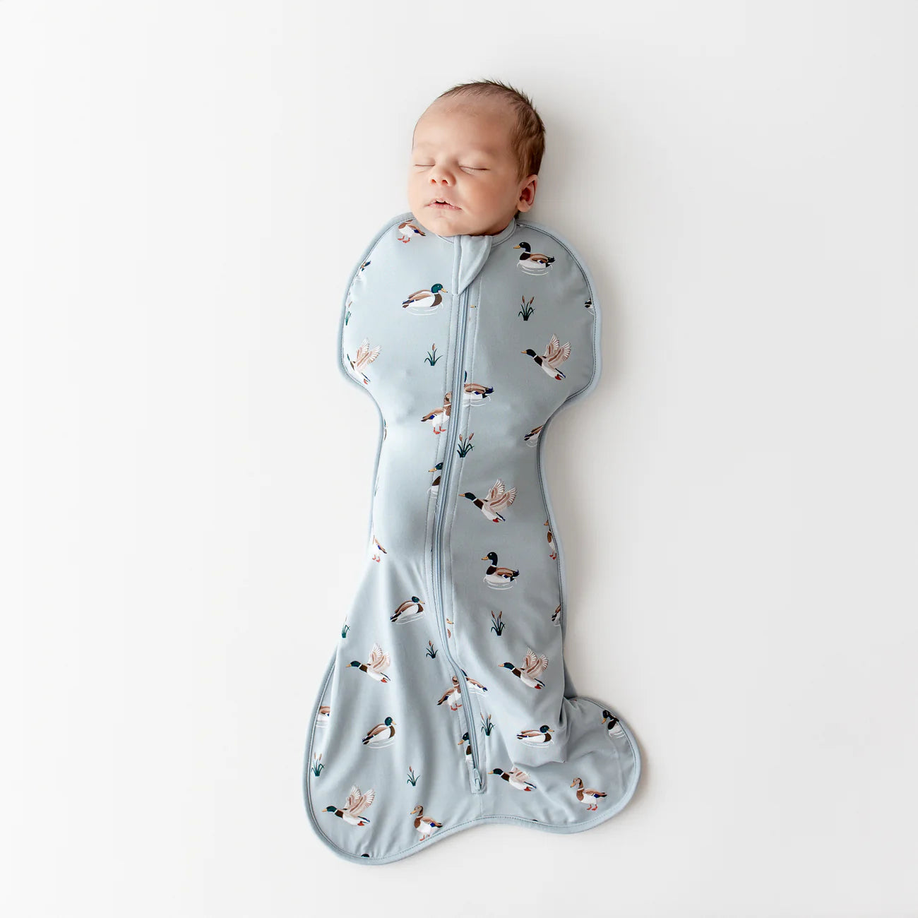 Baby sleeping in a light blue swaddle with duck pattern on a white background