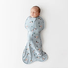 Baby sleeping in a light blue swaddle with duck pattern on a white background
