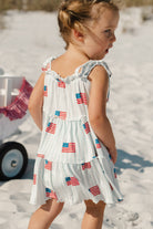 Child wearing a light blue and white striped dress with American flag patterns 