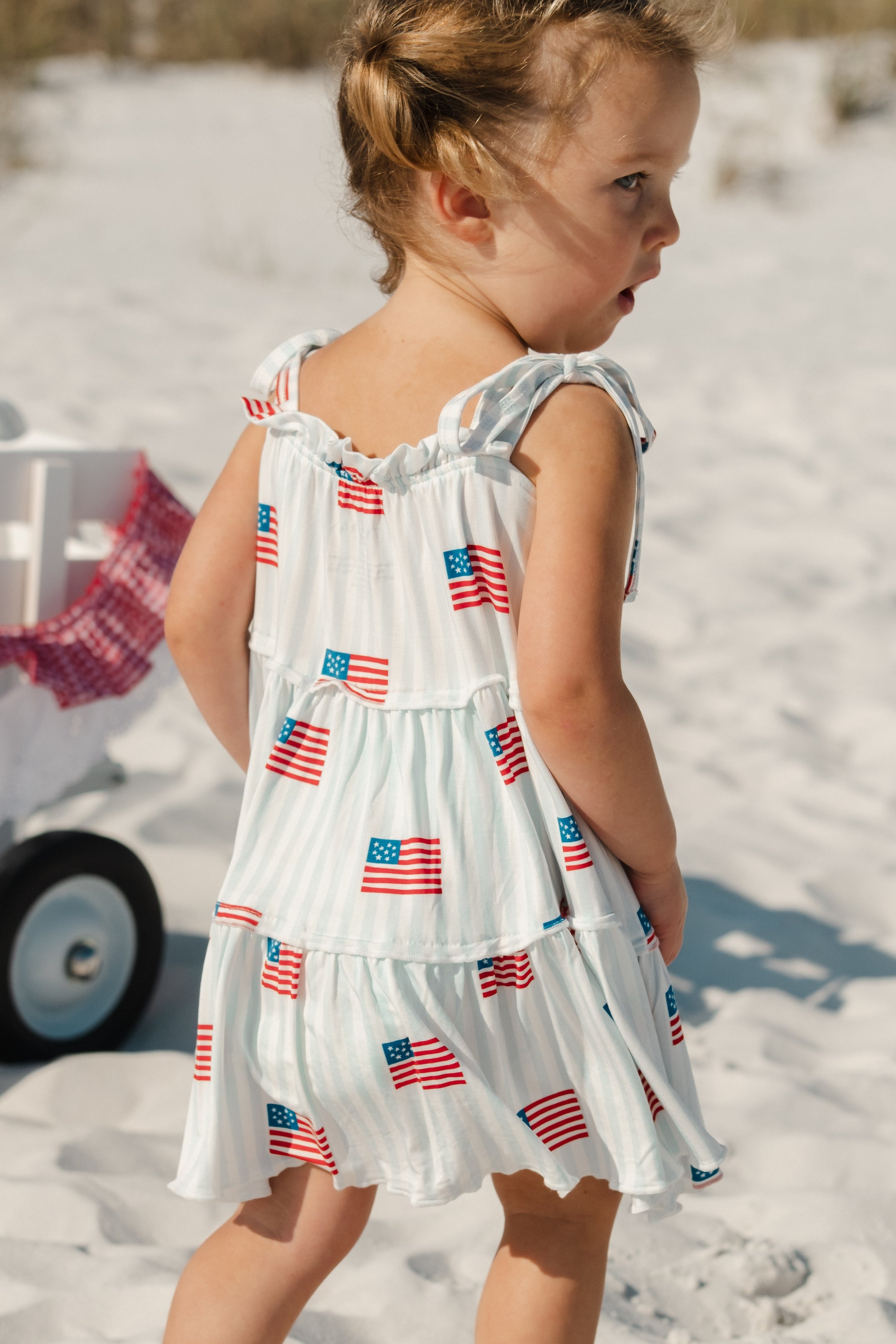 Child wearing a light blue and white striped dress with American flag patterns 