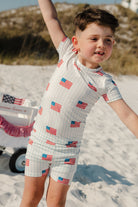 Child wearing a blue and white striped short sleeve pajama set with an American flag pattern