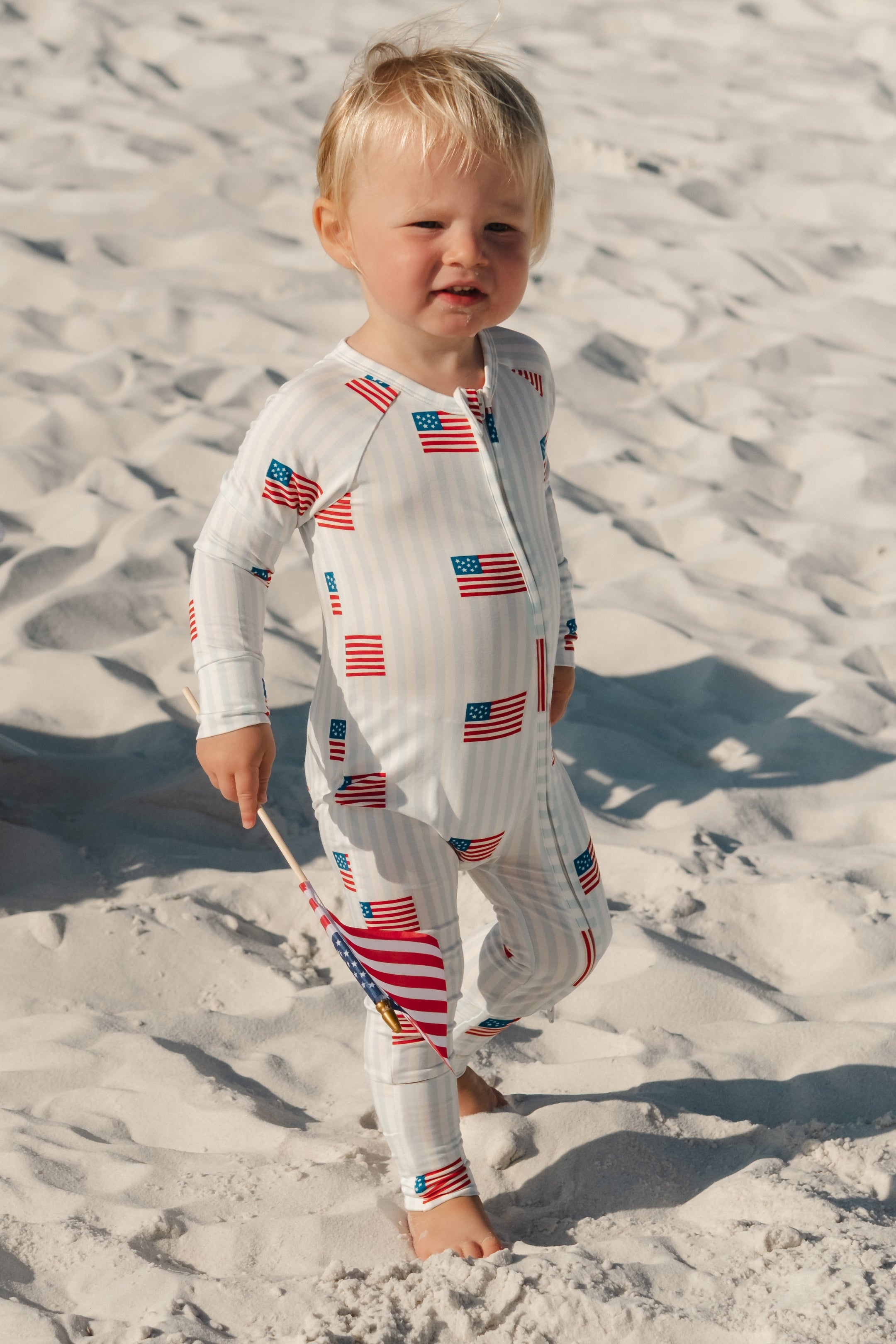 Baby onesie with light blue and white stripes, with American flag patterns. 