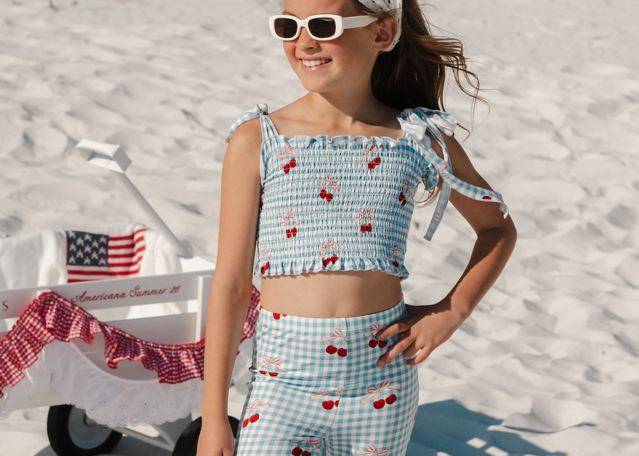 Young girl in a blue and red patterned outfit standing on a sandy beach.