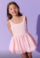 Young girl wearing a pink dress with pink gems on the neckline against a purple background