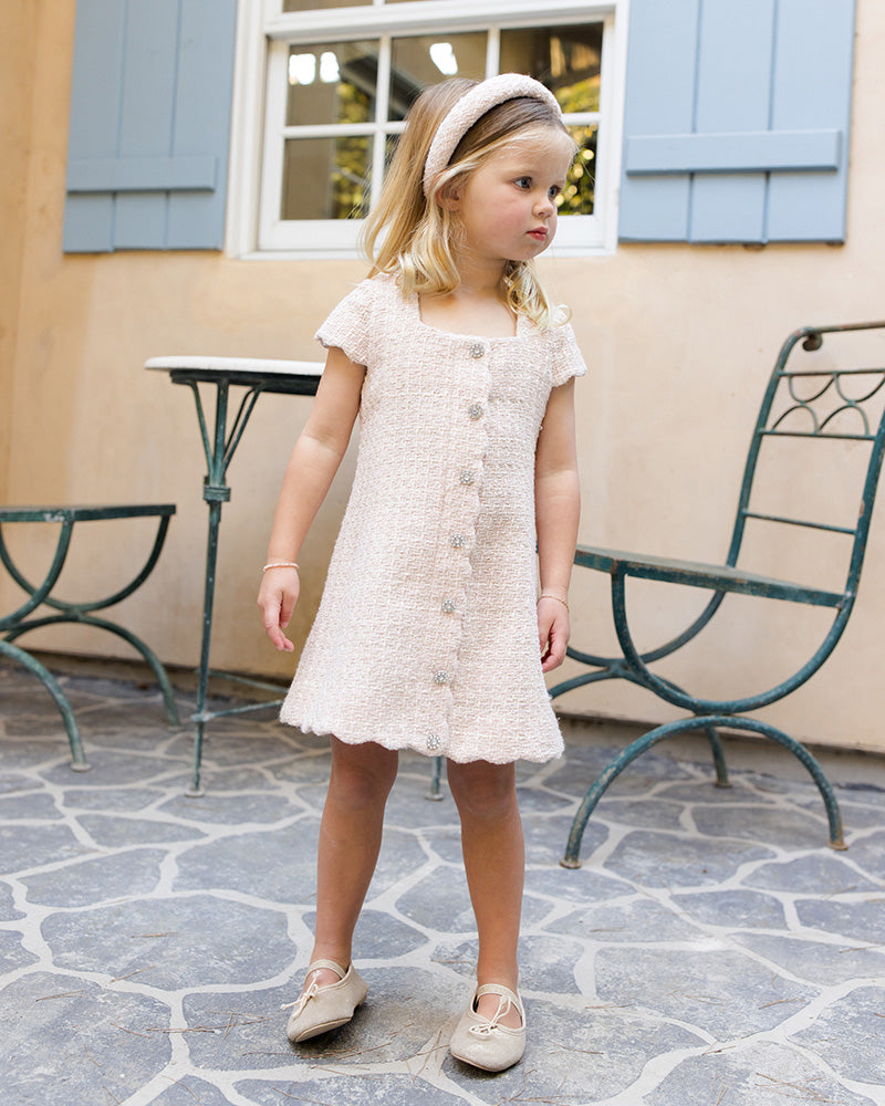 Young girl in a white lace dress standing on a stone patio.