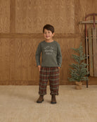 Child wearing a long-sleeve boxy shirt with text against a wooden wall