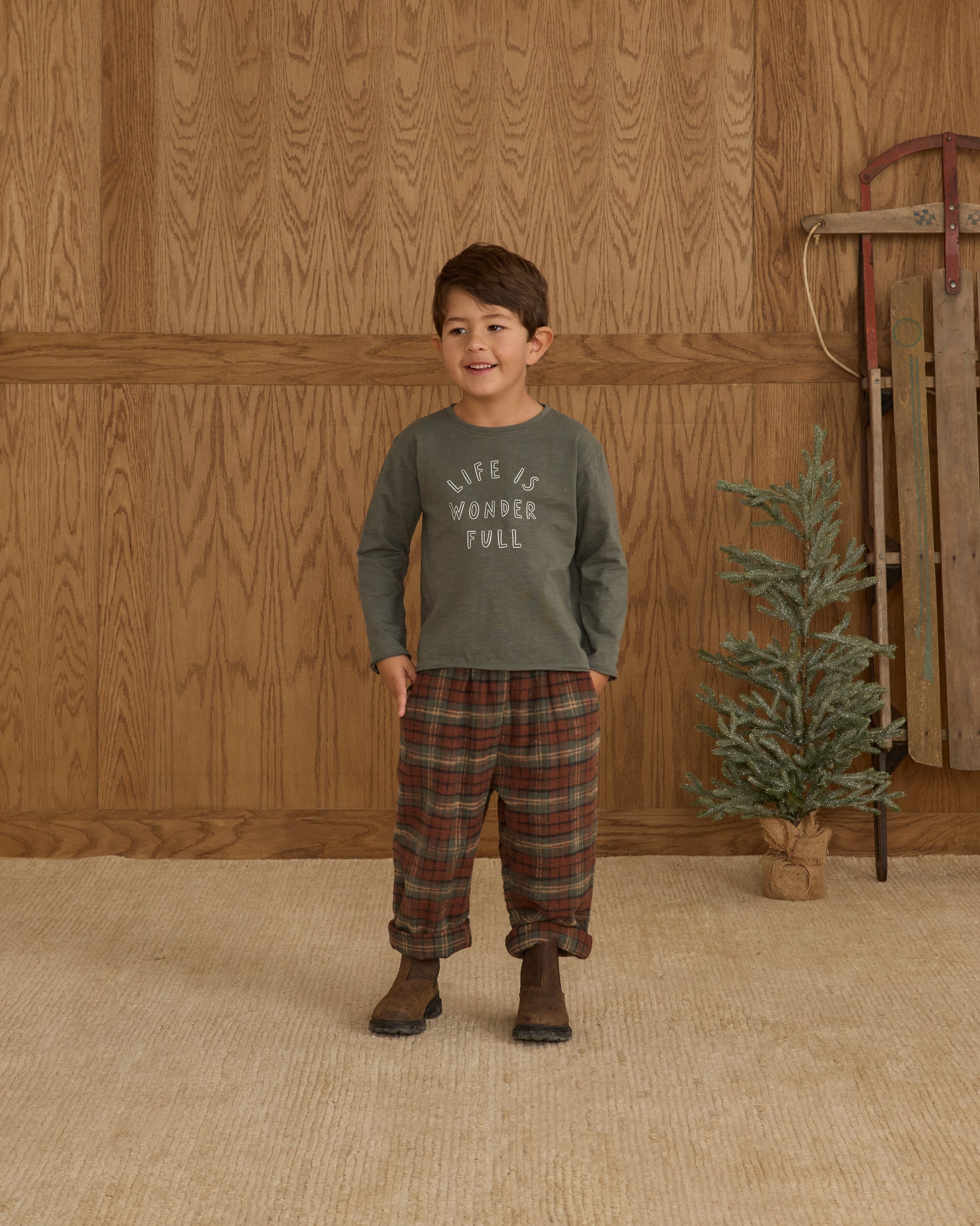 Child wearing a long-sleeve boxy shirt with text against a wooden wall