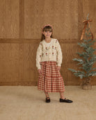 Young girl in a boxy crop cardigan with a red floral pattern and buttons. 