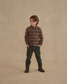 Child wearing a holiday plaid button up against a beige wall. 