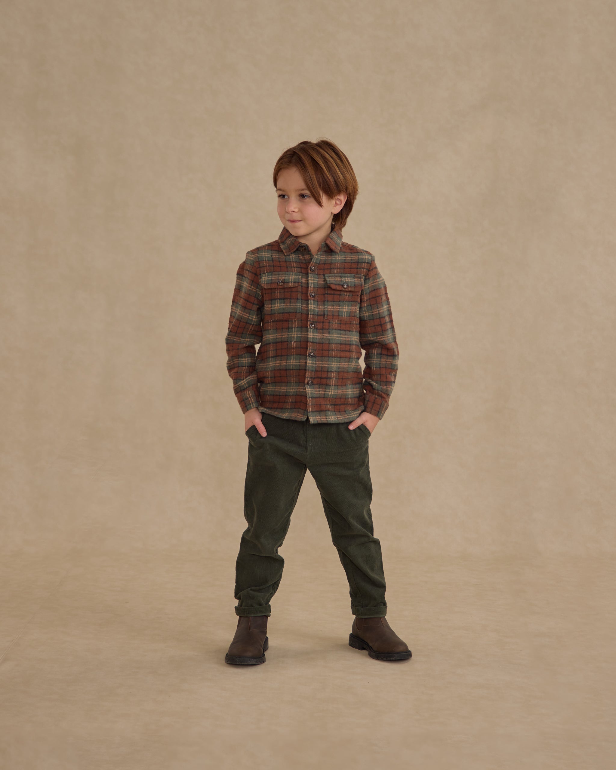 Child wearing a holiday plaid button up against a beige wall. 