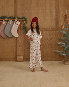 Child wearing a floral pajama set with stockings and a Christmas tree in the background.