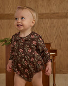 Baby wearing a floral onesie standing in front of a wooden background
