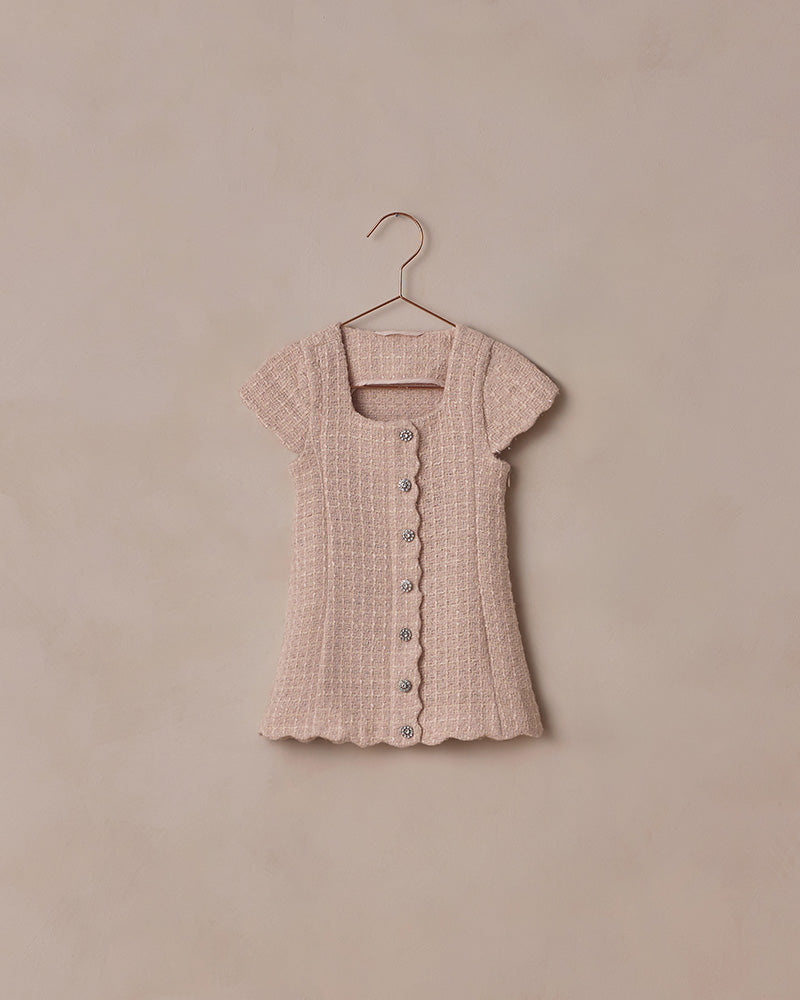 Pink textured dress on a hanger against a beige background