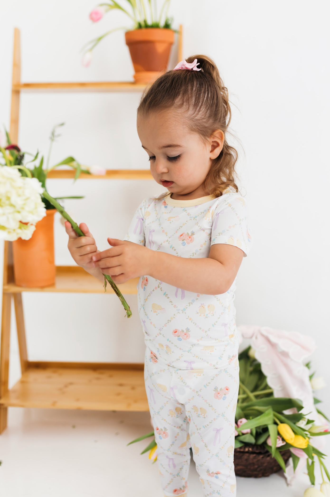 Child in a pajama set with a floral and bow pattern holding flowers.