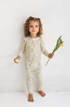 Child wearing floral patterned pajamas holding a tulip against a white background