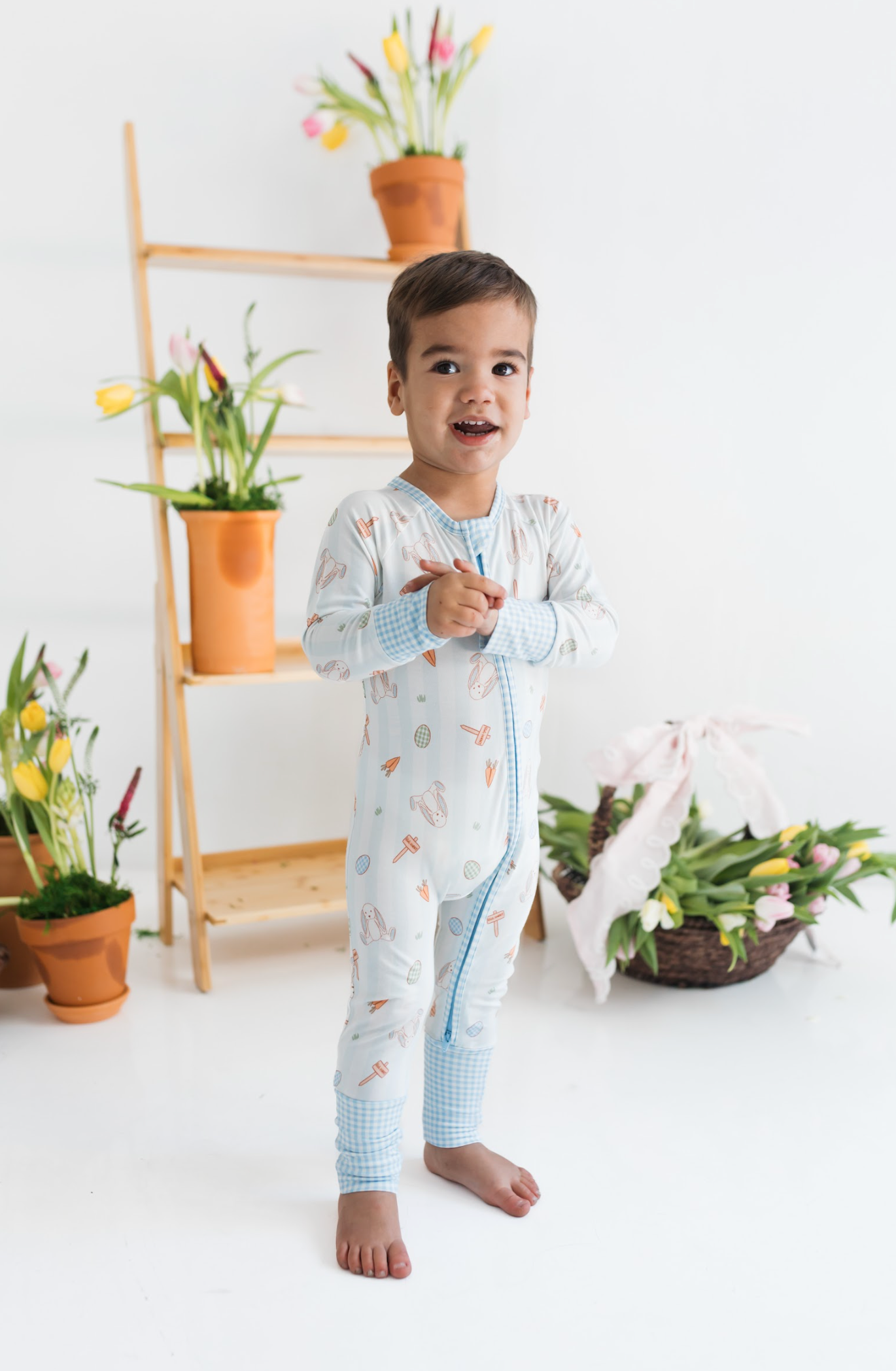 Child wearing a light blue pajama set with animal and easter prints in a room with plants and flowers.