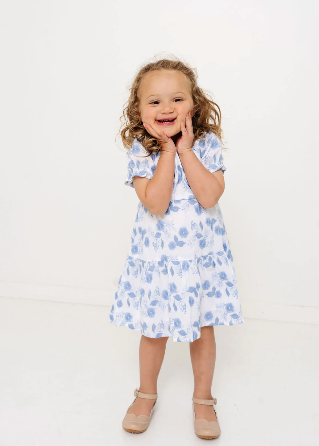 Young girl wearing a white dress with blue floral pattern against a white background