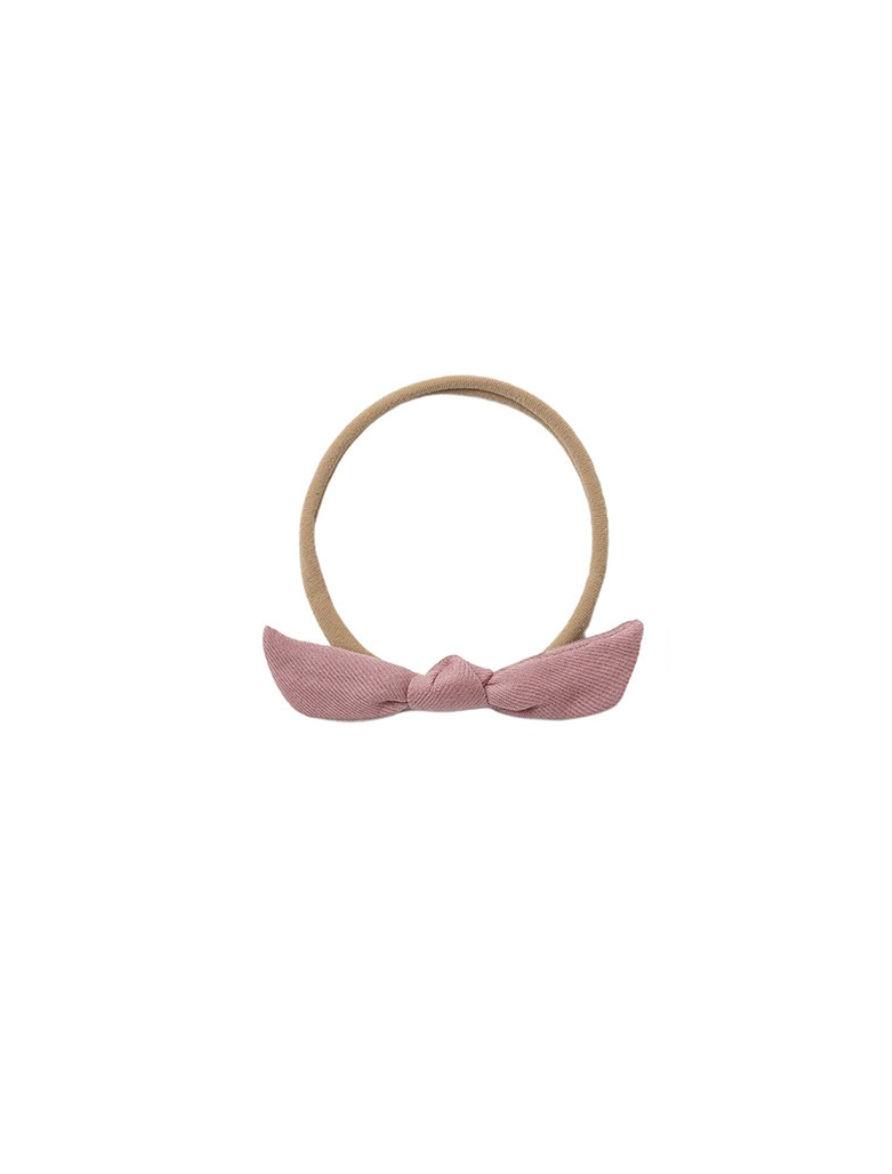 A beige fabric headband with a dusty pink bow at the front, displayed against a solid white background.