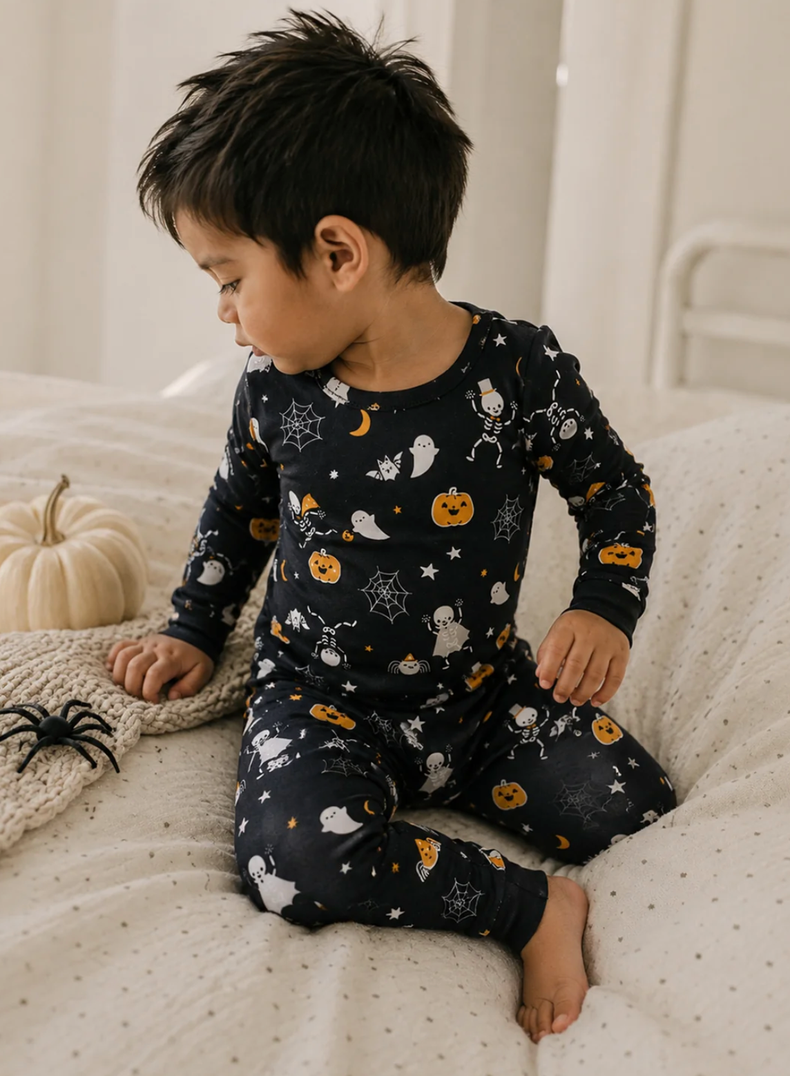 A two-piece children's pajama set featuring a long-sleeve top and matching pants in black with a Halloween print of orange pumpkins, white ghosts, spiders, and moons.