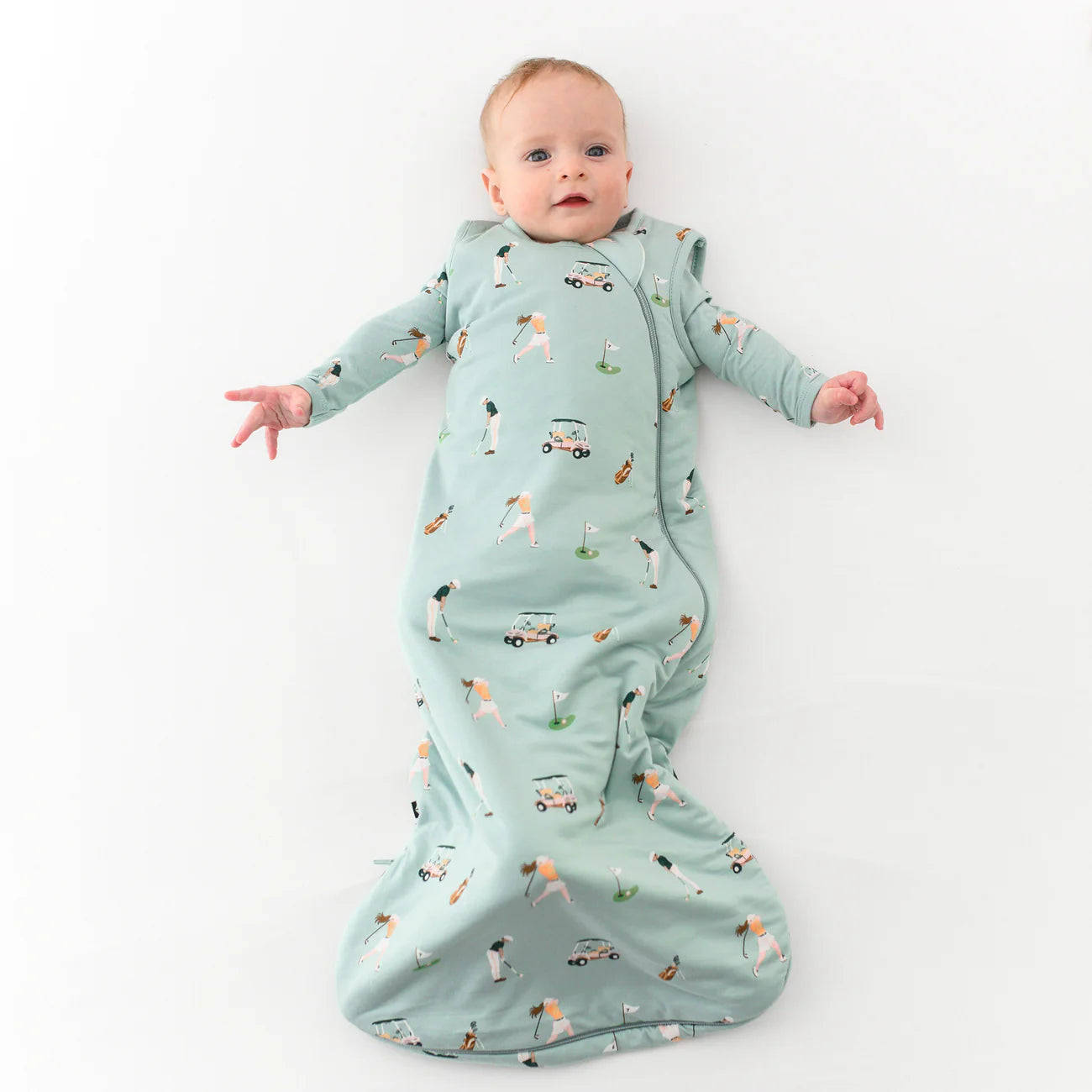 Baby in a light blue sleep sack with printed golf design on a white background