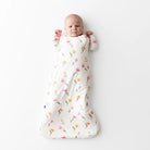 Baby wrapped in a floral-patterned sleep sack on a white background