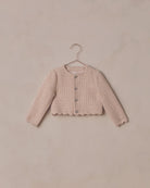 Pink textured cardigan on a hanger against a beige background