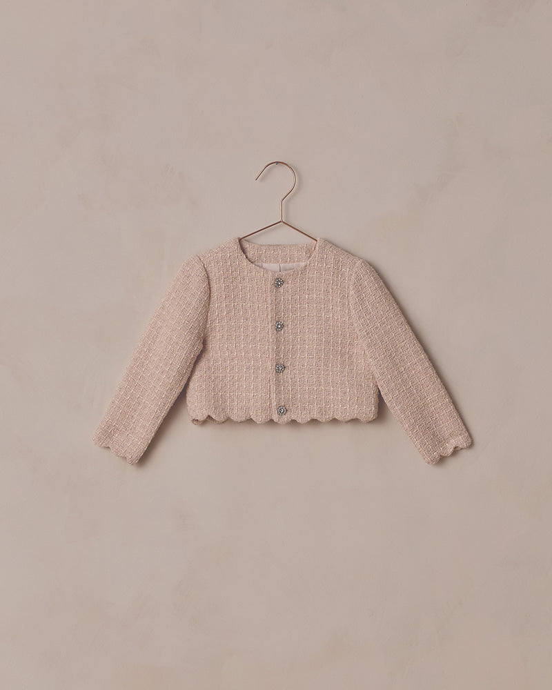 Pink textured cardigan on a hanger against a beige background