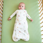 Baby lying on a green mattress in a crib with a floral-patterned sleep sack.