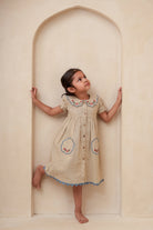 Young girl in a beige dress with floral patterns standing inside an archway.