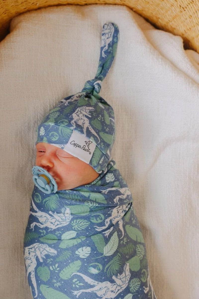 baby swaddled in dinosaur and leaf print swaddle and matching hat 