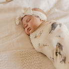 baby swaddled in horse print swaddle with matching bow 