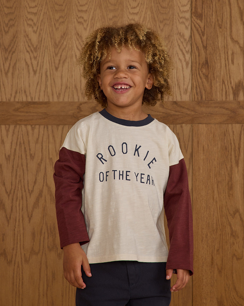 Child wearing a 'Rookie of the Year' shirt against a wooden background