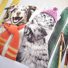 Cat wearing a pink knitted hat and orange scarf next to a dog on a colorful background