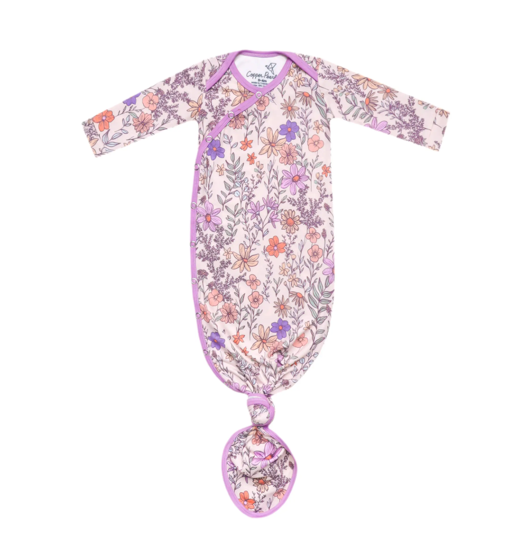 A floral-patterned newborn knotted gown in shades of pink and purple with long sleeves and a bottom knot for diaper changes.