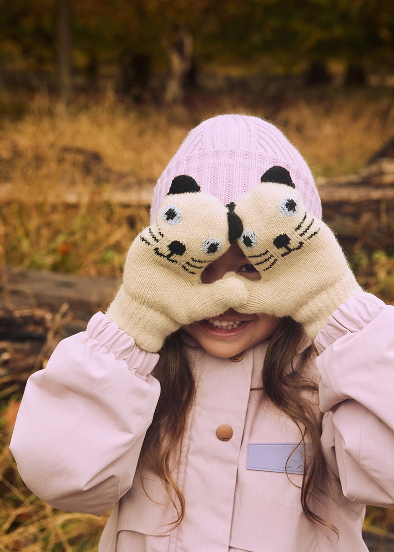 Child wearing cat-themed mittens and a pink hat in an outdoor setting