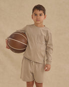 Child holding a basketball wearing a beige outfit on a beige background