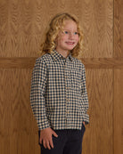 Child wearing a navy checkered shirt against a wooden paneled wall