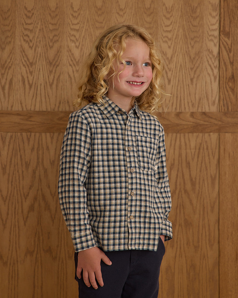 Child wearing a navy checkered shirt against a wooden paneled wall