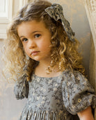 Young girl with curly hair wearing a floral dress and headband in an elegant interior setting.