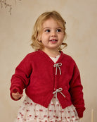 Child wearing a red knitted cardigan with bow details against a beige background
