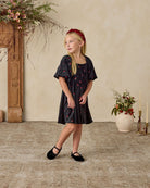 Young girl in a black floral dress standing in a room with decorative elements.