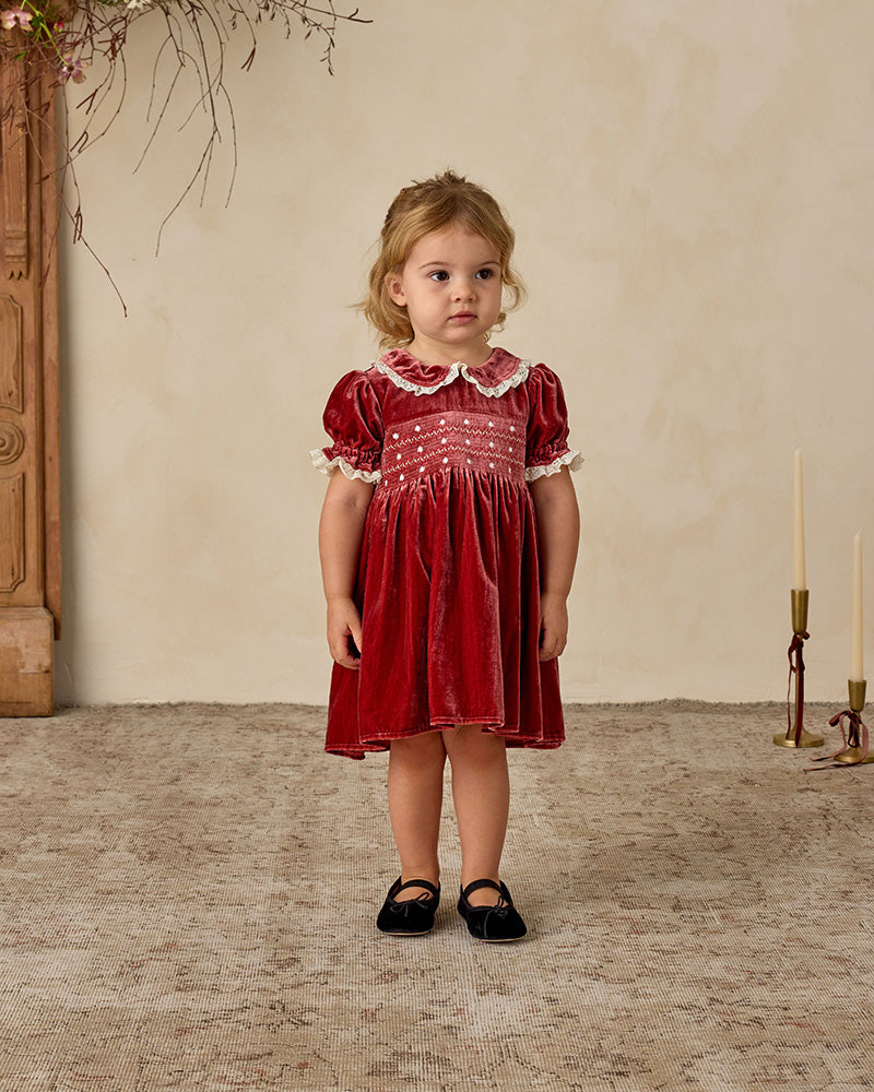 Young girl in a red velvet dress with white detailing and ruffled sleeves with a neutral background